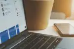 white laptop computer turned on beside brown paper cup